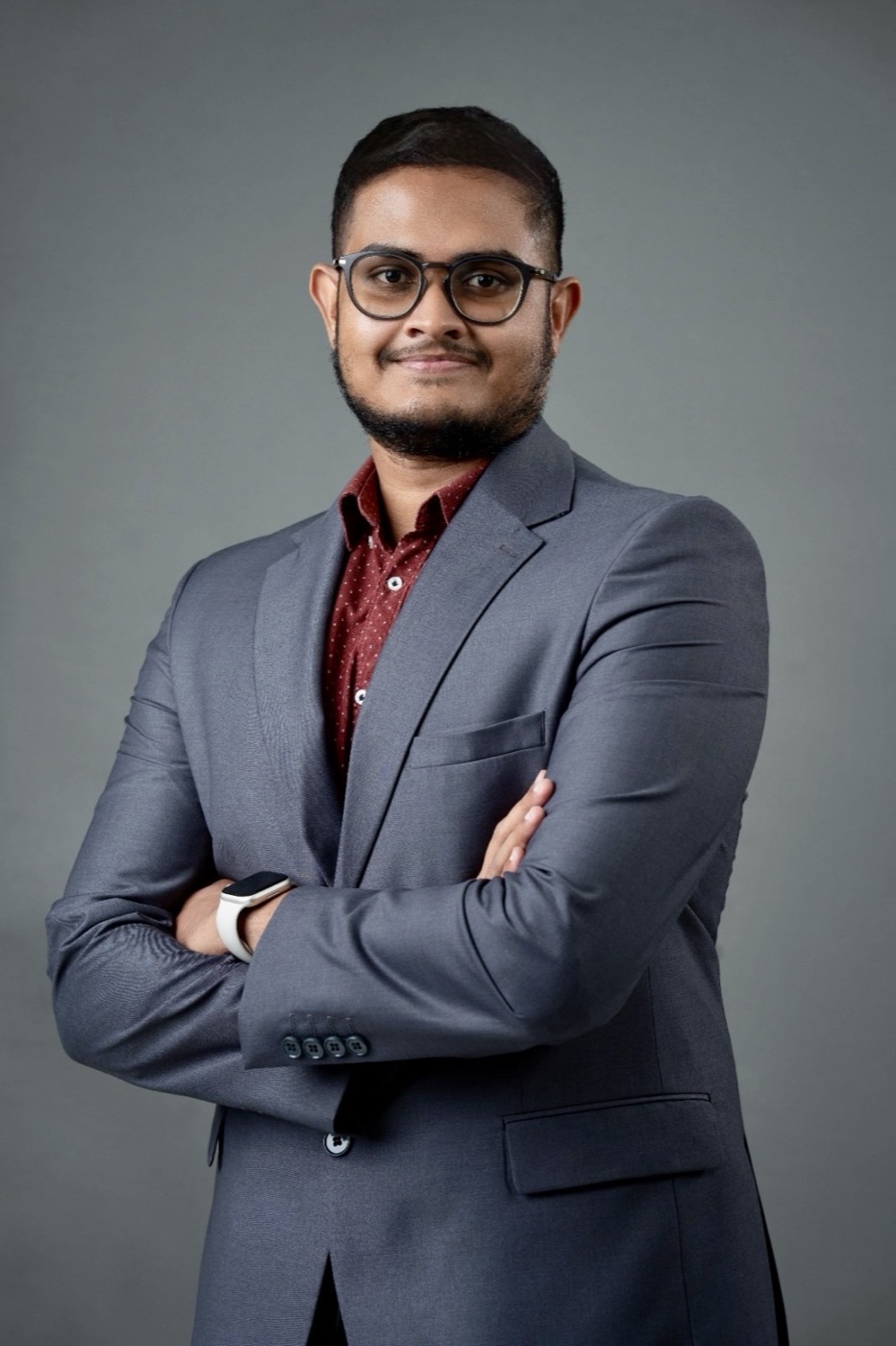 Enura Indula in a grey suit, arms folded, smiling