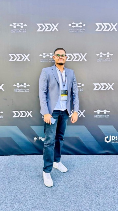Enura in a light blazer with a lanyard in front of an event backdrop