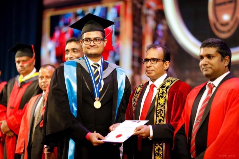 Enura in graduation robes receiving a certificate on stage