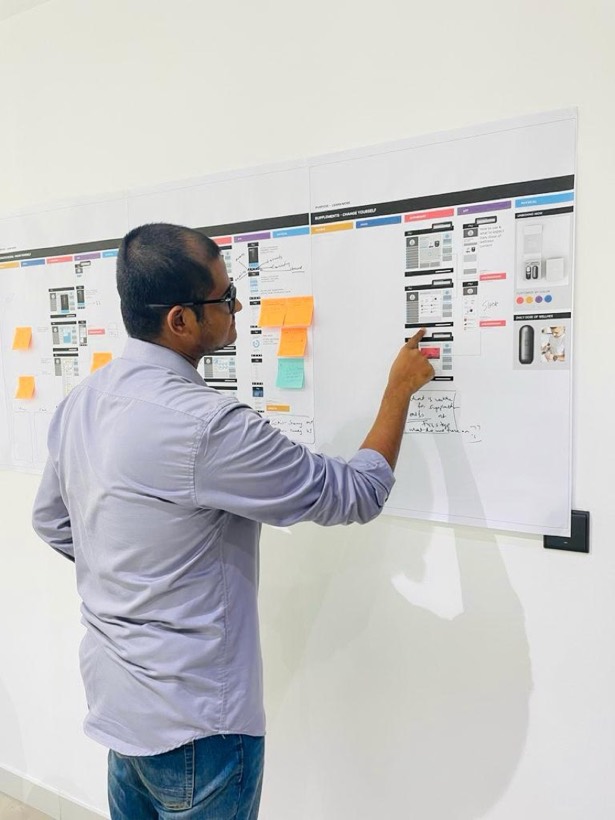 Enura at a whiteboard covered in printed screens and orange sticky notes